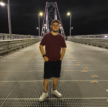 Foto de Leonardo com camisa bordô, óculos ,short jeans preto,com tenis branco